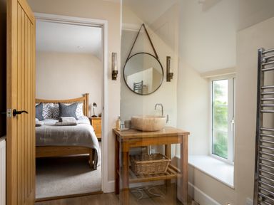 A bathroom with a wooden sink table and round mirror next to a bedroom with a wooden bed at Orchard House in Stow-On-The-Wold