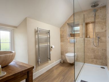 A bathroom with a wooden countertop and stone sink a wall-mounted towel rack toilet and a glass-enclosed shower at Orchard House in Stow-On-The-Wold