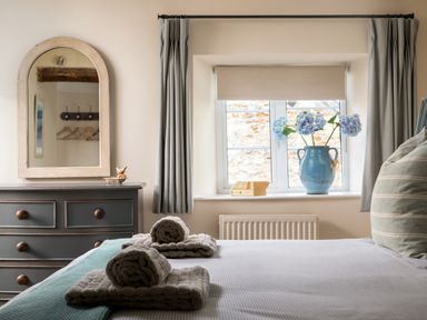 A bedroom with a bed folded towels a dresser with a mirror and a window with flowers at Orchard House in Stow-On-The-Wold