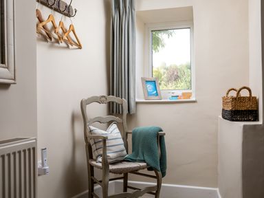 A corner with a wooden chair with a cushion and blanket near a window with books and a photo frame at Orchard House in Stow-On-The-Wold