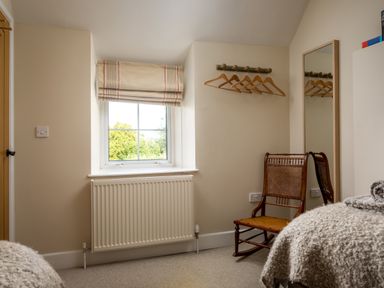 A bedroom corner with a window radiator wooden chair wall-mounted hangers and a tall mirror at Orchard House in Stow-On-The-Wold