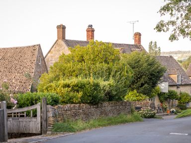 A rural street with stone houses chimneys bushes and a wooden gate at Orchard House in Stow-On-The-Wold
