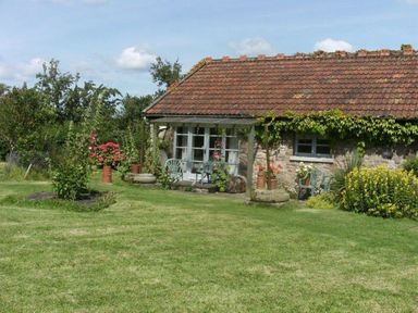 A stone cottage with a tiled roof and garden furniture surrounded by plants and flowers on a lawn at The Piggery in Lydney