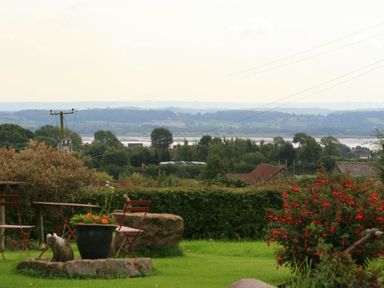 A garden with chairs and a flower pot overlooking trees and hills at The Piggery in Lydney