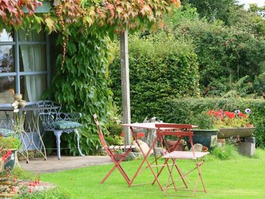 A garden with a metal table and chairs on the grass next to a house covered in climbing plants at The Piggery in Lydney