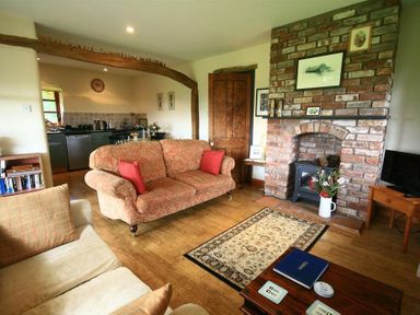 A living room with sofas a brick fireplace and an open kitchen at The Piggery in Lydney