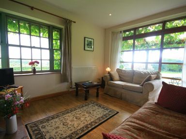 A living room with two sofas a coffee table a television and large windows with curtains at The Piggery in Lydney
