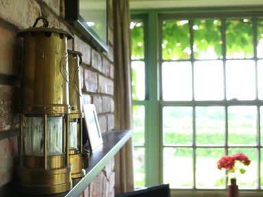 A shelf with brass lanterns and a framed photo next to a window with a view of greenery and flowers