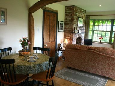 A dining table with four chairs and flowers beside a wooden door and brick fireplace in a living room at The Piggery in Lydney