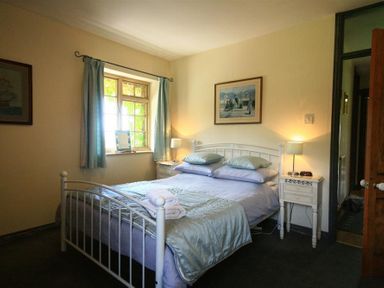 A bedroom with a metal bed frame two bedside tables with lamps a window with curtains and framed pictures on the walls at The Piggery in Lydney