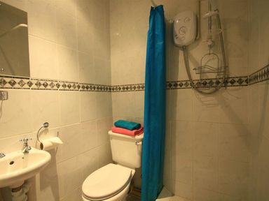 A bathroom with a toilet sink shower with blue curtain and folded towels on the toilet tank at The Piggery in Lydney