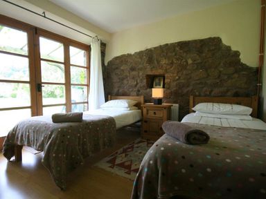 A bedroom with two single beds a wooden nightstand and a stone wall at The Piggery in Lydney