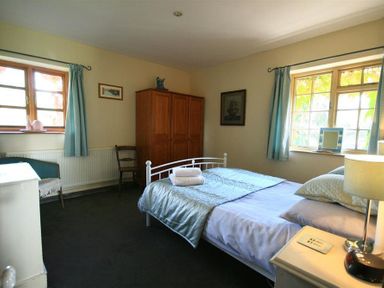 A bedroom with a bed a wardrobe a chair and windows with blue curtains at The Piggery in Lydney