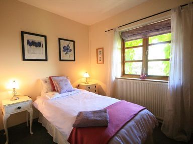 A bedroom with a bed and two bedside tables with lamps and a window with curtains at The Piggery in Lydney