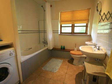 A bathroom with a bathtub shower washing machine toilet and sink at The Piggery in Lydney