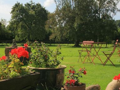 A garden with red flowers in pots and a table with chairs on green grass at The Piggery in Lydney