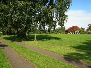 A grassy field with a tree and a house covered in ivy in the distance at The Piggery in Lydney