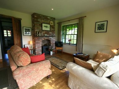 A living room with a brick fireplace couches and a window with curtains at The Piggery in Lydney