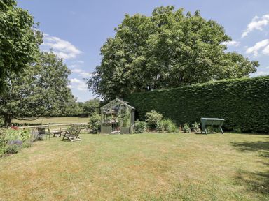 A garden with a greenhouse and garden furniture at The Old Reading Room Bledington near Stow-on-the-Wold