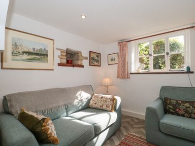 A sitting room with two sofas a lamp paintings on the wall and a window with curtains at Mayfly Cottage Coln St Aldwyns near Bibury