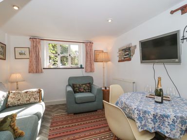 A living room with sofa armchair table with blue floral tablecloth and wall mounted TV at Mayfly Cottage Coln St Aldwyns near Bibury