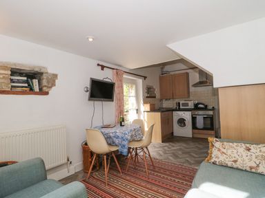 A kitchen and dining area with a small table and chairs a mounted TV and a washing machine at Mayfly Cottage in Coln St Aldwyns near Bibury