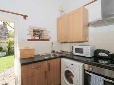 A kitchen with wooden cabinets a washing machine a microwave a toaster and a bread box at Mayfly Cottage in Coln St Aldwyns near Bibury