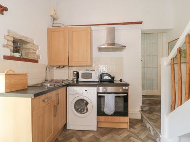 A kitchen with wooden cabinets a washing machine oven microwave toaster and a bread box at Mayfly Cottage in Coln St Aldwyns near Bibury