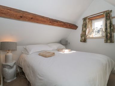 A bedroom with a double bed under a wooden beam and small window at Mayfly Cottage in Coln St Aldwyns near Bibury