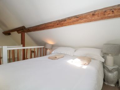 A bedroom with a double bed bedside lamps and exposed wooden beams at Mayfly Cottage in Coln St Aldwyns near Bibury