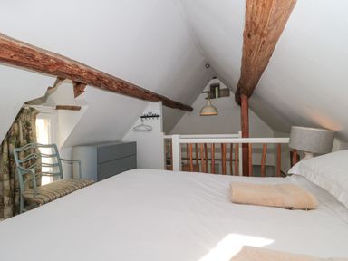 A bedroom with a bed a chair a chest of drawers and exposed wooden beams at Mayfly Cottage in Coln St Aldwyns near Bibury