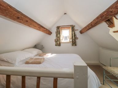 A bedroom with a double bed and wooden beams on the ceiling at Mayfly Cottage Coln St Aldwyns near Bibury