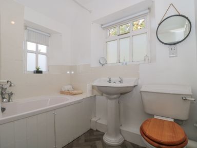 A bathroom with a bathtub sink toilet and two windows at Mayfly Cottage in Coln St Aldwyns near Bibury