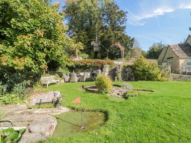 A garden with a miniature golf course bench and outdoor dining furniture at Mayfly Cottage Coln St Aldwyns near Bibury