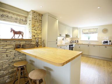 A kitchen with wooden countertops stools and stone wall at Old Groom's Cottage in Minster Lovell
