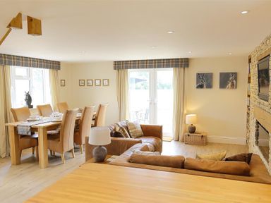 A living room with leather sofas a wooden dining table with chairs and a wall mounted TV at Old Groom's Cottage in Minster Lovell