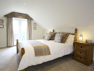 A bedroom with a wooden bed and matching bedside table with a lamp at Old Groom's Cottage in Minster Lovell