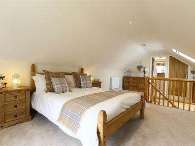 A bedroom with a wooden bed, matching side tables, and a wooden dresser at Old Groom's Cottage in Minster Lovell