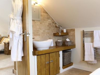 A bathroom with a wooden vanity holding a white sink and wicker baskets with towels and a towel rack with white towels at Old Groom's Cottage Minster Lovell