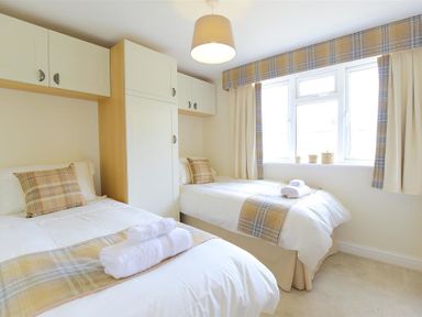 A bedroom with two single beds two windows and built in cupboards at Old Groom's Cottage in Minster Lovell