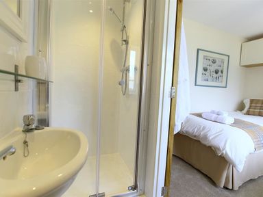 A small bathroom with a washbasin and shower next to a bedroom with a bed and folded towels at Old Groom's Cottage in Minster Lovell