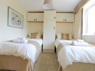 A bedroom with two single beds with plaid pillows and blankets with built-in storage cabinets above and between the beds at Old Groom's Cottage in Minster Lovell