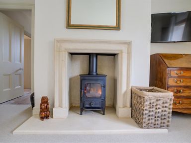 A fireplace with a wood burning stove a wooden bear figure a wicker basket and a wooden chest of drawers at The Old Dairy in Shilton