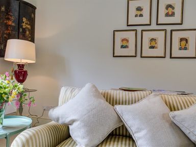 A striped sofa with three cushions next to a side table with flowers and a lamp and framed pictures on a wall at The Old Dairy in Shilton