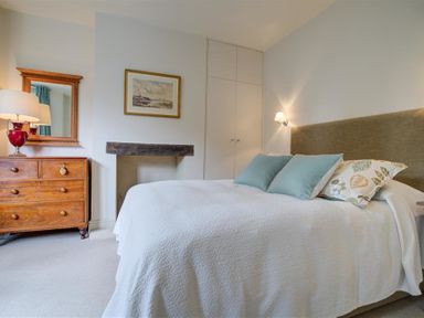 A bedroom with a bed white bedding pillows wooden dresser mirror and built in cupboards at The Old Dairy in Shilton
