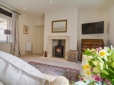 A living room with a wood stove fireplace a television on the wall and flowers on a table at The Old Dairy in Shilton