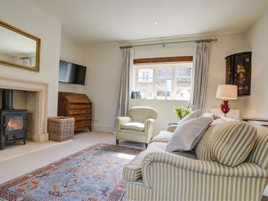A living room with a striped sofa armchair fireplace and television at The Old Dairy in Shilton