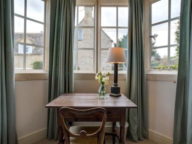A wooden table with a lamp and flowers in front of windows with green curtains at The Old Dairy in Shilton