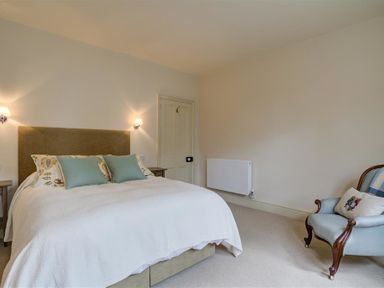 A bedroom with a double bed with pillows and bedside tables a door a radiator and an armchair at The Old Dairy in Shilton