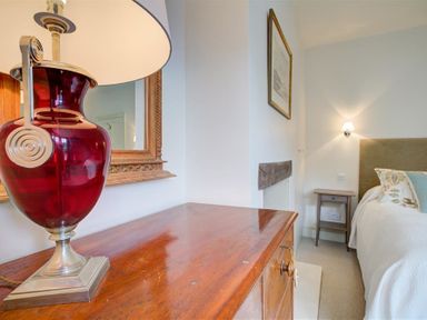 A bedroom with a wooden dresser and red lamp next to a bed with cushions at The Old Dairy in Shilton